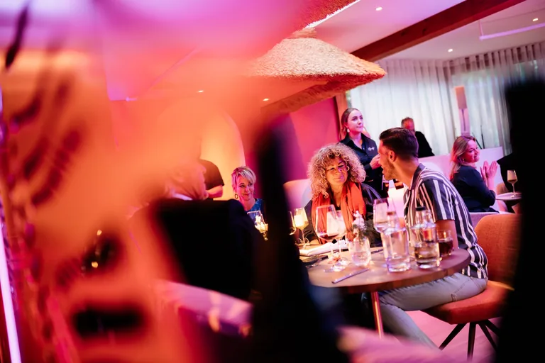 Een gezelschap aan tafel in Restaurant Amante, met warme roze en oranje verlichting.