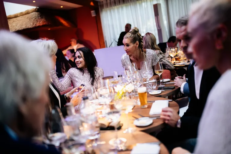 Gasten aan een lange gedekte tafel met wijnglazen en warme sfeerverlichting.