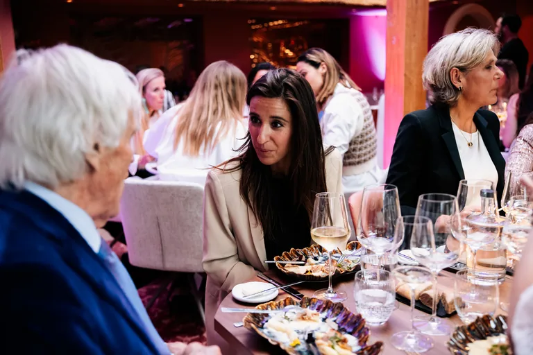 Gasten in gesprek aan een gedekte tafel met gerechten en wijnglazen.