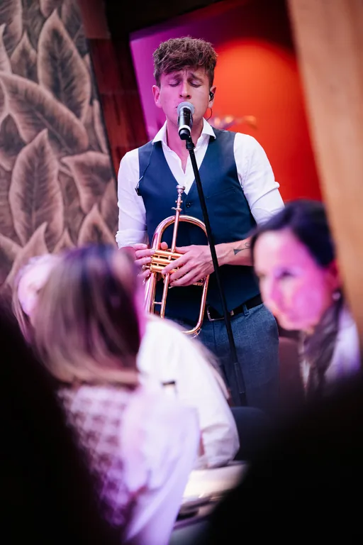 Een muzikant met een koperblaasinstrument staat bij een microfoon tussen de gasten.