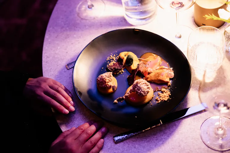 Bovenaanzicht van een opgemaakt gerecht op een donker bord, met glaswerk en bestek ernaast.