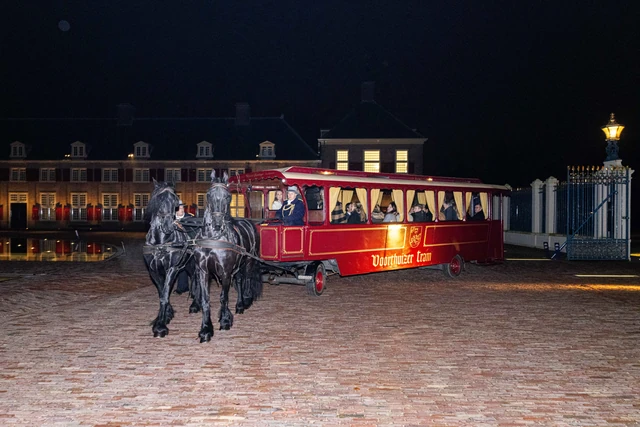 Twee paarden met een rode paardentram bij een verlichte entree.