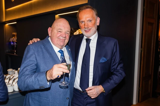 Twee gasten poseren samen; een van hen houdt een glas vast.