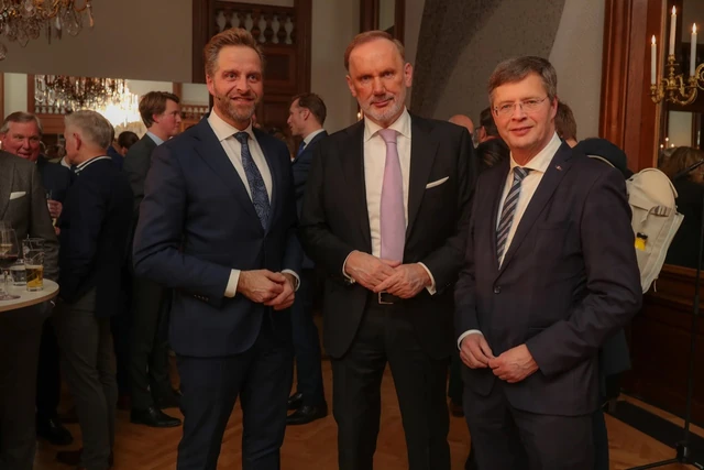 Drie gasten poseren samen, met andere gasten op de achtergrond.