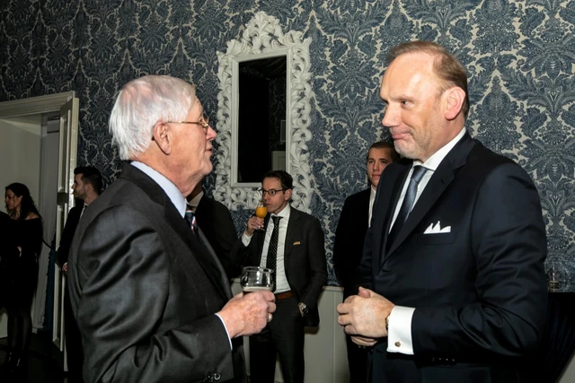 Twee gasten staan met elkaar in gesprek, met andere gasten op de achtergrond.