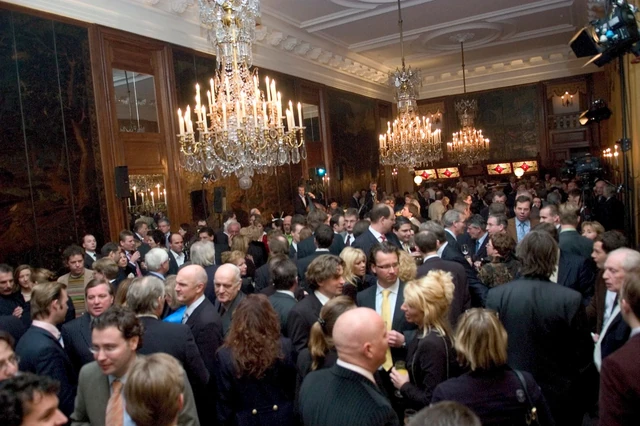 Een overzicht van een zaal vol gasten onder grote kroonluchters.