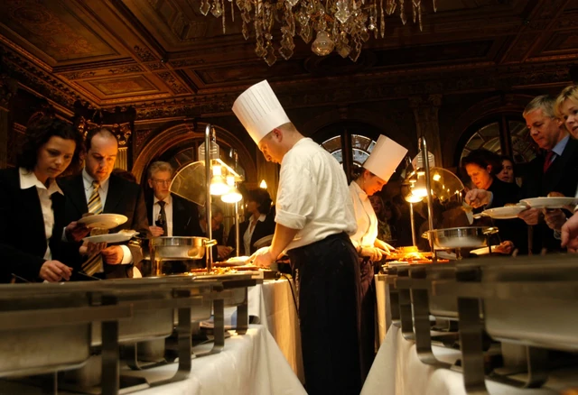 Gasten staan met borden bij een warm verlicht buffet.