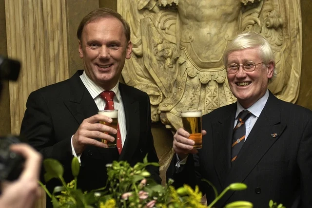 Twee gasten houden een glas omhoog naast een bloemstuk.
