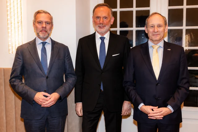 Drie gasten poseren naast elkaar bij hoge ramen tijdens een nieuwjaarsreceptie.