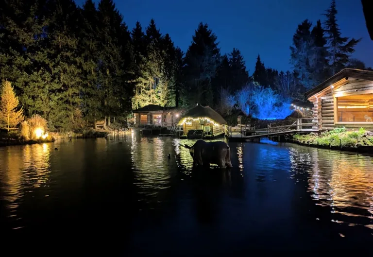 Avondsfeer bij Sauna Drôme in Putten, met verlichte saunagebouwen en weerspiegelingen op het water.