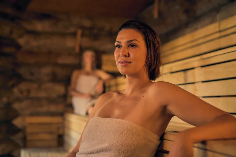 Een gast met een handdoek op een houten bank in de sauna.