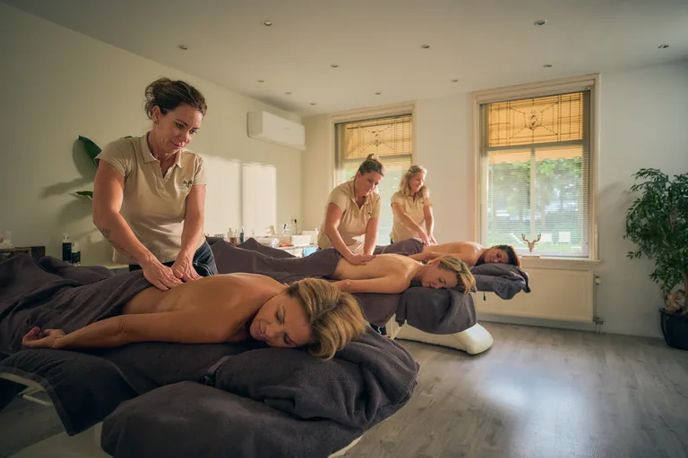 Gasten krijgen een massage in een lichte behandelruimte.
